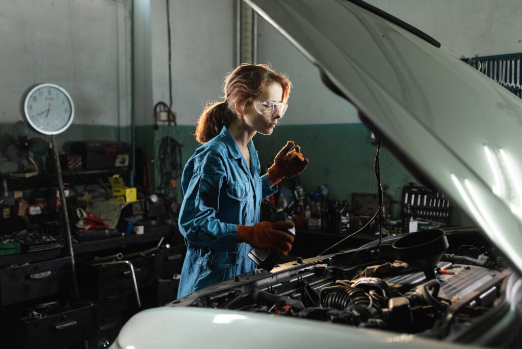 auto repair shop and worker locksmith girl pours oil or tossol. The concept of servicing cars and auto engines in the garage. Women's profession and workwear. Open hood of the car.